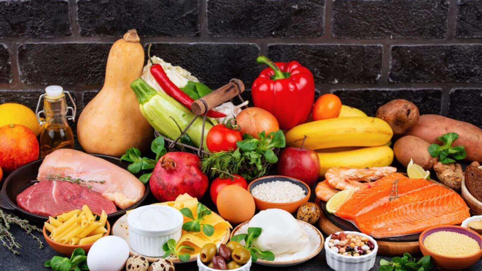Mesa com alimentos frescos e variados, incluindo frutas, vegetais, carnes, peixes e grãos, destacando uma dieta balanceada e saudável.