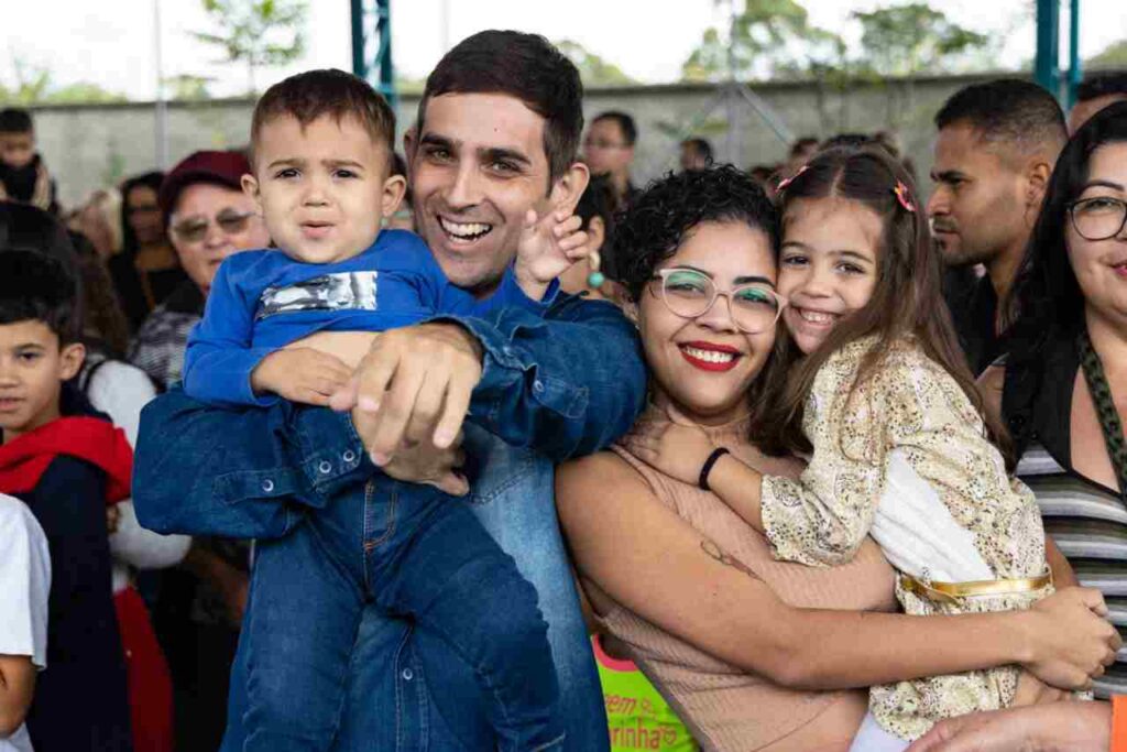 Família sorridente aproveita evento na EMEB Luzia Francisca, Jundiaí, celebrando apresentação teatral "Eu Tenho Voz" com alegria e união.