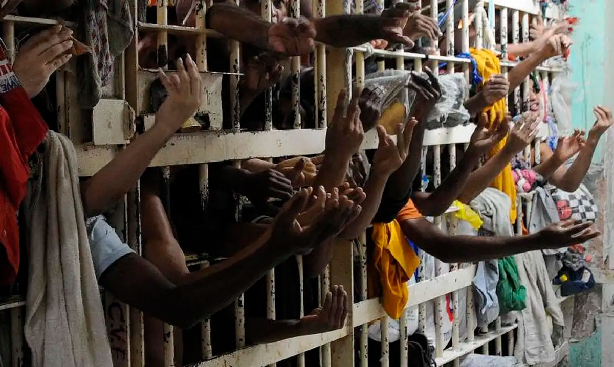 Cela superlotada de presídio, com vários detentos com os braços para fora das grades.