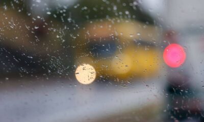 Gotas de chuva embaçam vidro, destacando luzes desfocadas de carros na rua em dia chuvoso em Jundiaí.