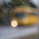 Gotas de chuva embaçam vidro, destacando luzes desfocadas de carros na rua em dia chuvoso em Jundiaí.