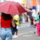 Mulher com guarda-chuva vermelho caminha em rua movimentada de Jundiaí em dia chuvoso, vestindo blusa vermelha e jeans em vias de Jundiaí.