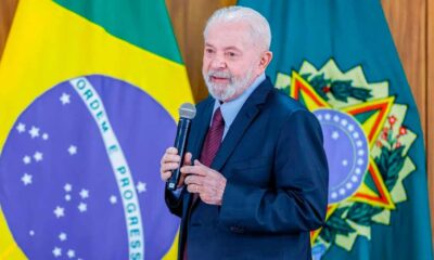 Presidente Lula falando ao microfone a frente da bandeira do Brasil