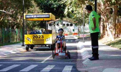 Criança andando de kart no Jardim da Mobilidade em Jundiaí, supervisionada por um instrutor. Atividade do Maio Amarelo
