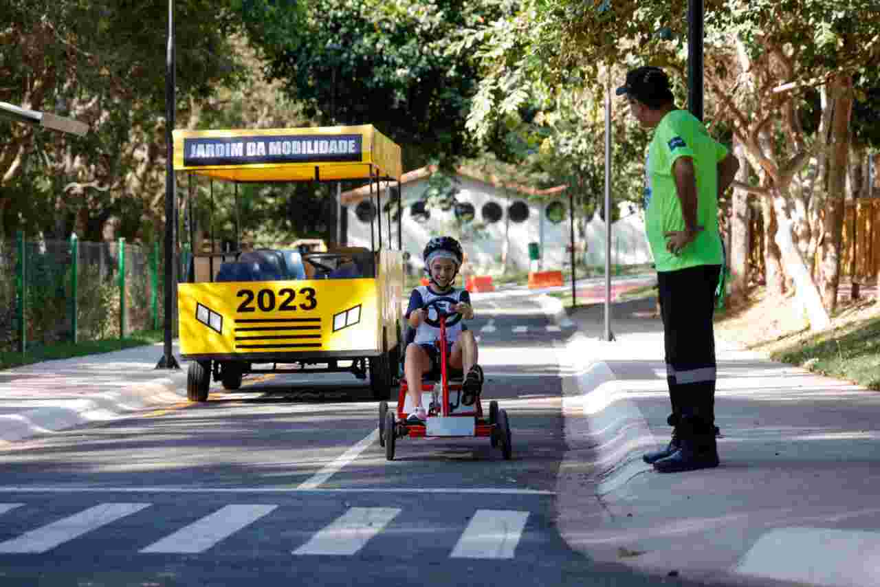 Criança andando de kart no Jardim da Mobilidade em Jundiaí, supervisionada por um instrutor. Atividade do Maio Amarelo