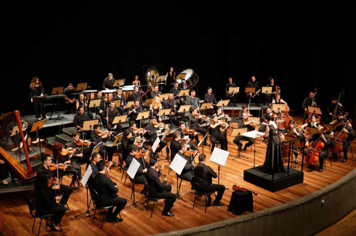 Grupo de pessoas com instrumentos musicais em cima de palco da Orquestra Sinfônica de Jundiaí
