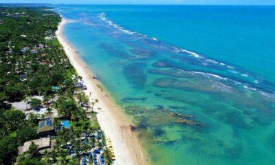 Praia paradisíaca em Trancoso, Bahia, com águas cristalinas, faixa de areia extensa e vegetação exuberante ao longo da costa.