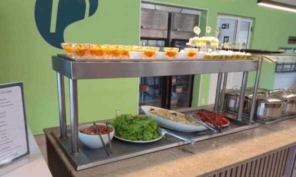 Buffet de saladas e sobremesas em restaurante, com cardápio do dia exposto, destacando ambiente moderno e organizado.