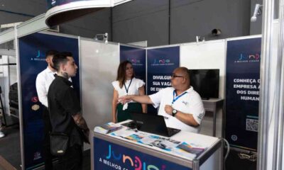 Stand da Prefeitura na Fatec Log 2024 na feira, com quatro pessoas conversando e banners de Jundiaí ao fundo, destacando oportunidades de emprego.