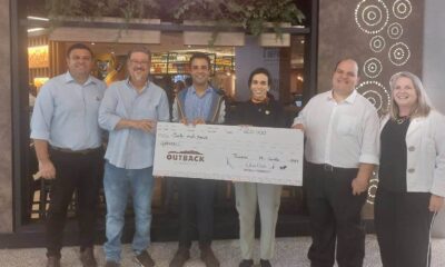 Pessoas segurando um cheque representando R$ 20 mil em gift cards do Outback do Maxi Shopping Jundiaí para o Grendacc