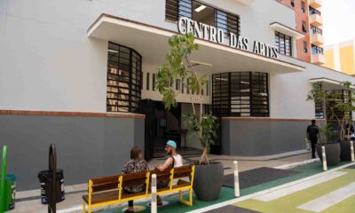 Entrada do Centro das Artes em Jundiaí, com duas pessoas sentadas em um banco na frente e plantas decorativas ao redor.