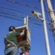 Homem instala câmeras de monitoramento em poste em Jundiaí, com fiação elétrica visível e céu azul ao fundo.