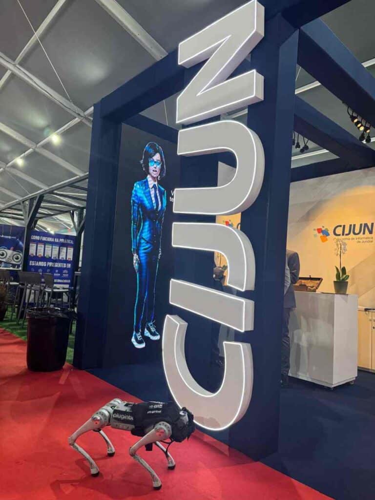 Stand da CIJUN com um cão-robô da Spot, da Boston Dynamics, em destaque em um evento tecnológico, com tela exibindo imagem digital.