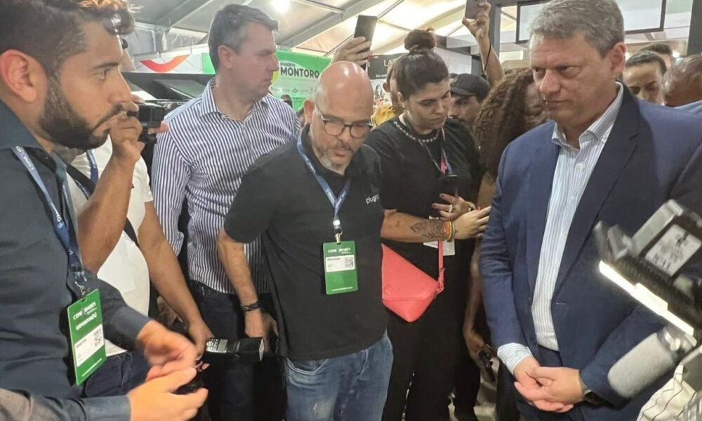 Autoridades e representantes da CIJUN discutem soluções tecnológicas em um evento, com várias pessoas ao fundo observando.