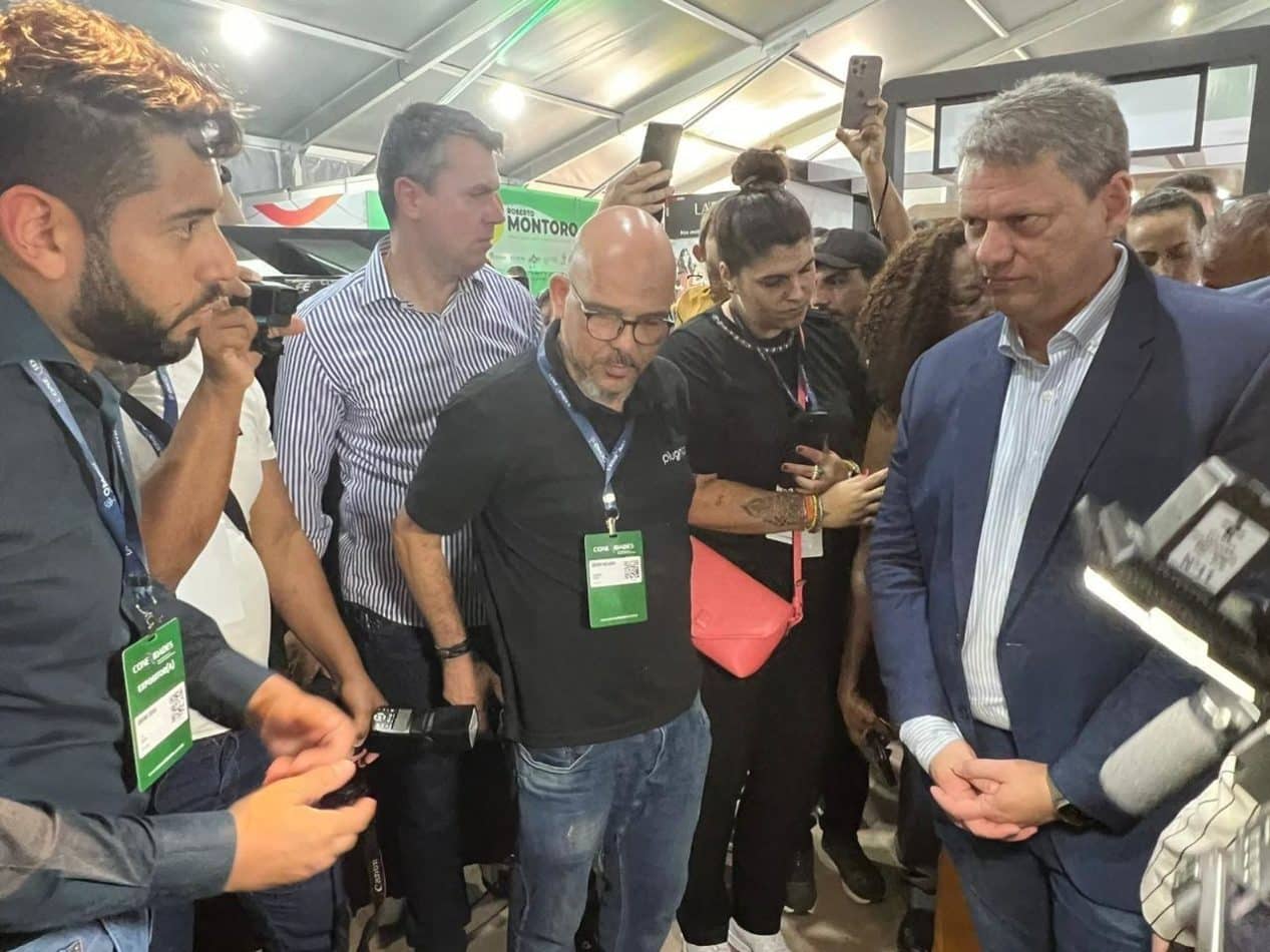 Autoridades e representantes da CIJUN discutem soluções tecnológicas em um evento, com várias pessoas ao fundo observando.