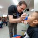 Profissional de saúde administra vacina oral contra poliomielite em uma criança, enquanto outras famílias aguardam na clínica.