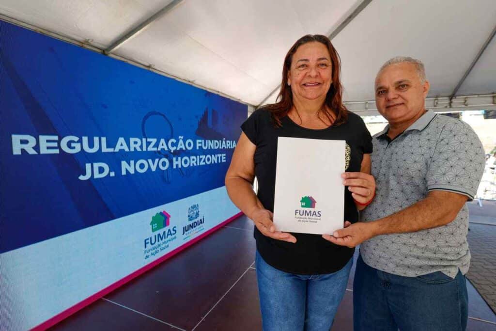 Entrega de escrituras no Jardim Novo Horizonte: Casal sorrindo com documento oficial em evento de regularização fundiária da FUMAS e Prefeitura de Jundiaí.