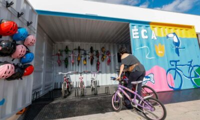 Imagem de uma mulher pegando uma bicicleta em uma bicicloteca de Jundiaí, que possui capacetes coloridos pendurados e bicicletas organizadas dentro de um contêiner decorado.