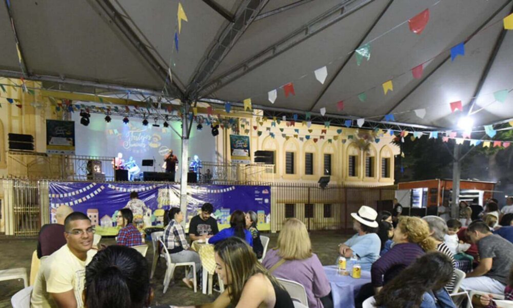 Decoração de festa junina na catedral do Centro de Jundiaí, com pessoas sentadas em cadeiras de plástico em volta de mesas