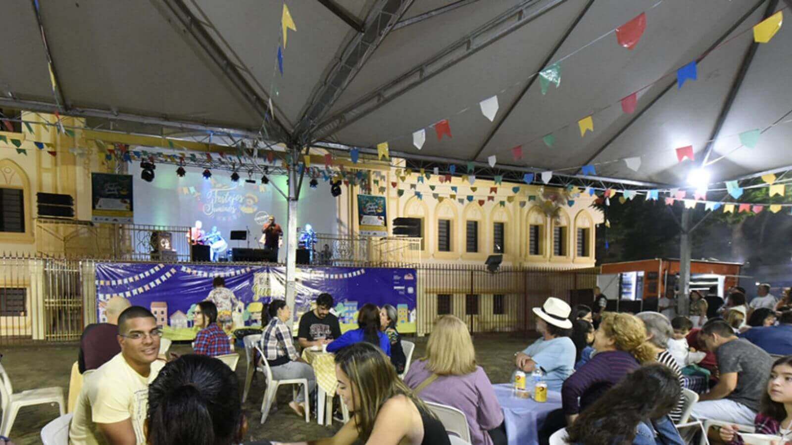 Decoração de festa junina na catedral do Centro de Jundiaí, com pessoas sentadas em cadeiras de plástico em volta de mesas