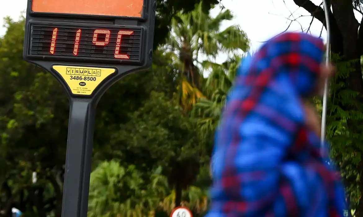 Temperaturas acima da média: Termômetro de rua mostra 11°C enquanto uma pessoa vestida com roupas de inverno caminha ao fundo.
