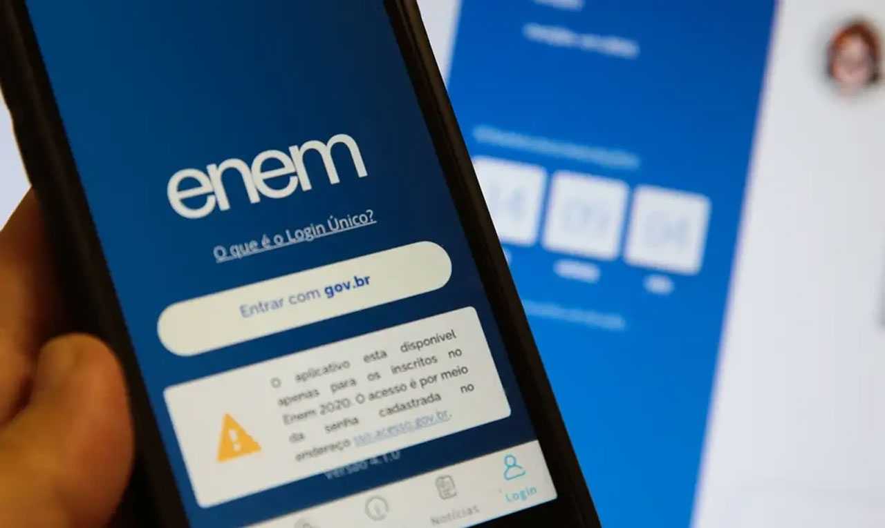 Uma mão segura um smartphone exibindo a tela de login das inscrições do ENEM 2024, com um fundo desfocado mostrando uma interface semelhante em uma tela maior.