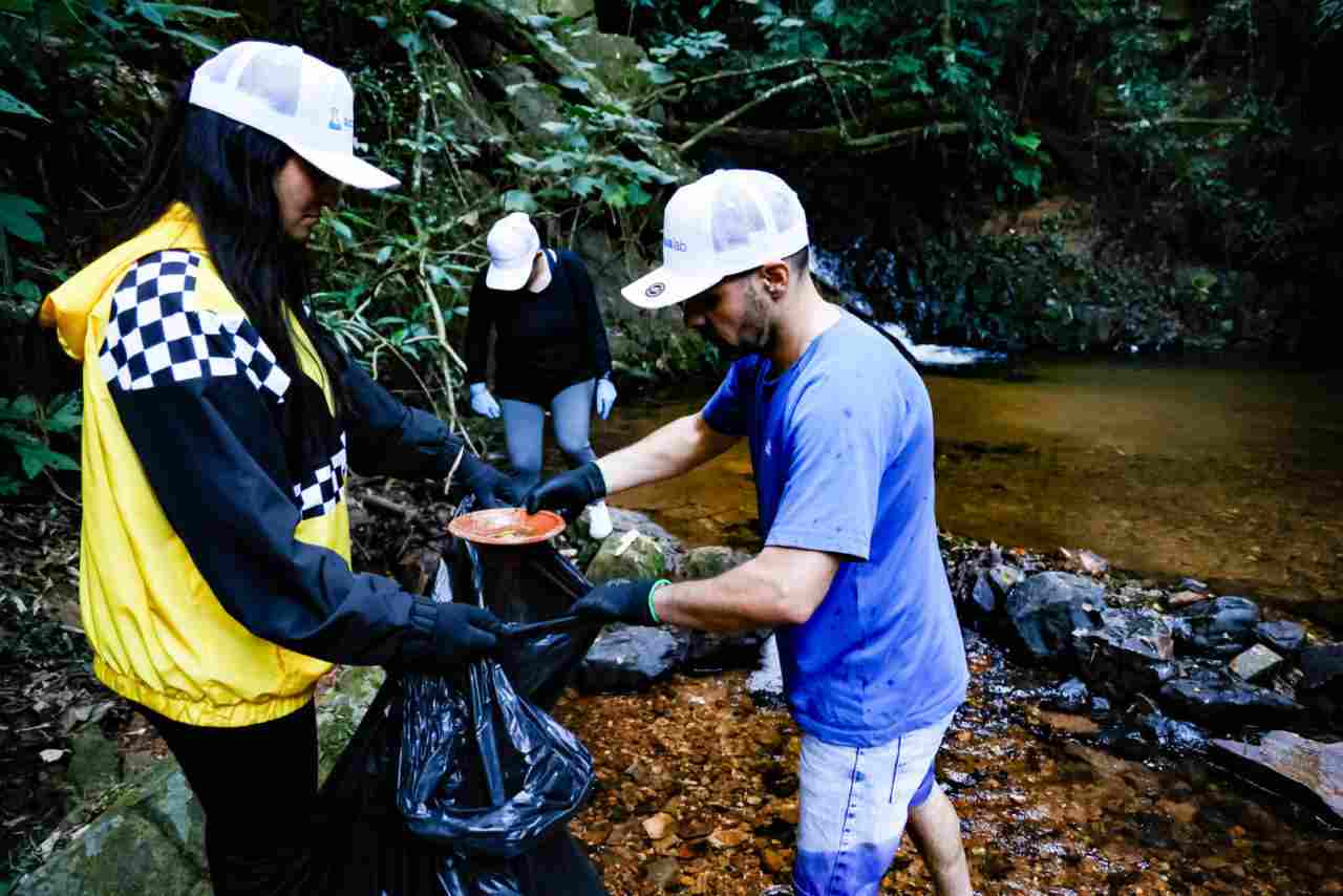 Voluntários realizando ação de limpeza na Serra do Japi, coletando lixo nas margens de um riacho em área florestal.