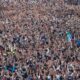 multidão participando da Marcha para Jesus 2024, com muitas pessoas de mãos levantadas, ao ar livre.