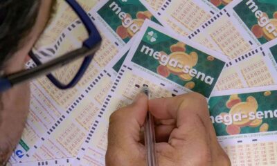 Homem marca números em bilhetes da Mega-Sena espalhados em mesa.