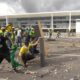 Manifestantes em frente à Praça dos Três Poderes, em Brasília, com alguns participantes jogando objetos e outros se protegendo com barricadas improvisadas nos atos golpistas de 8 de janeiro.