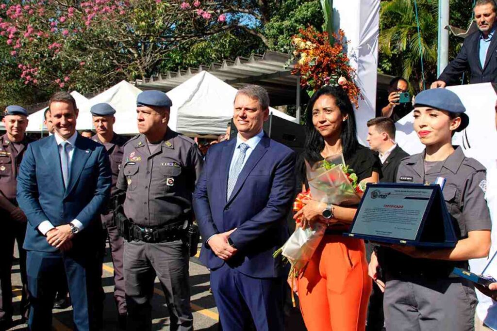 Cerimônia de formatura com autoridades e mulher premiada, destacando que Mulher passa em 1º lugar no curso da PM entre mais de mil soldados.