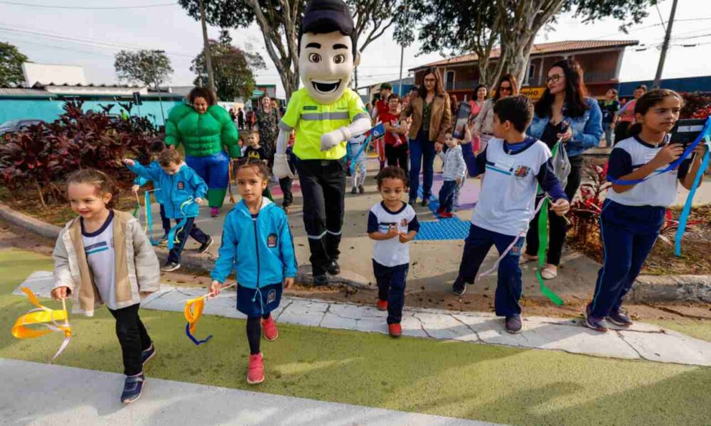 Crianças e adultos participam de uma atividade na Área da Infância em Jundiaí, acompanhadas por mascotes e segurando fitas coloridas.