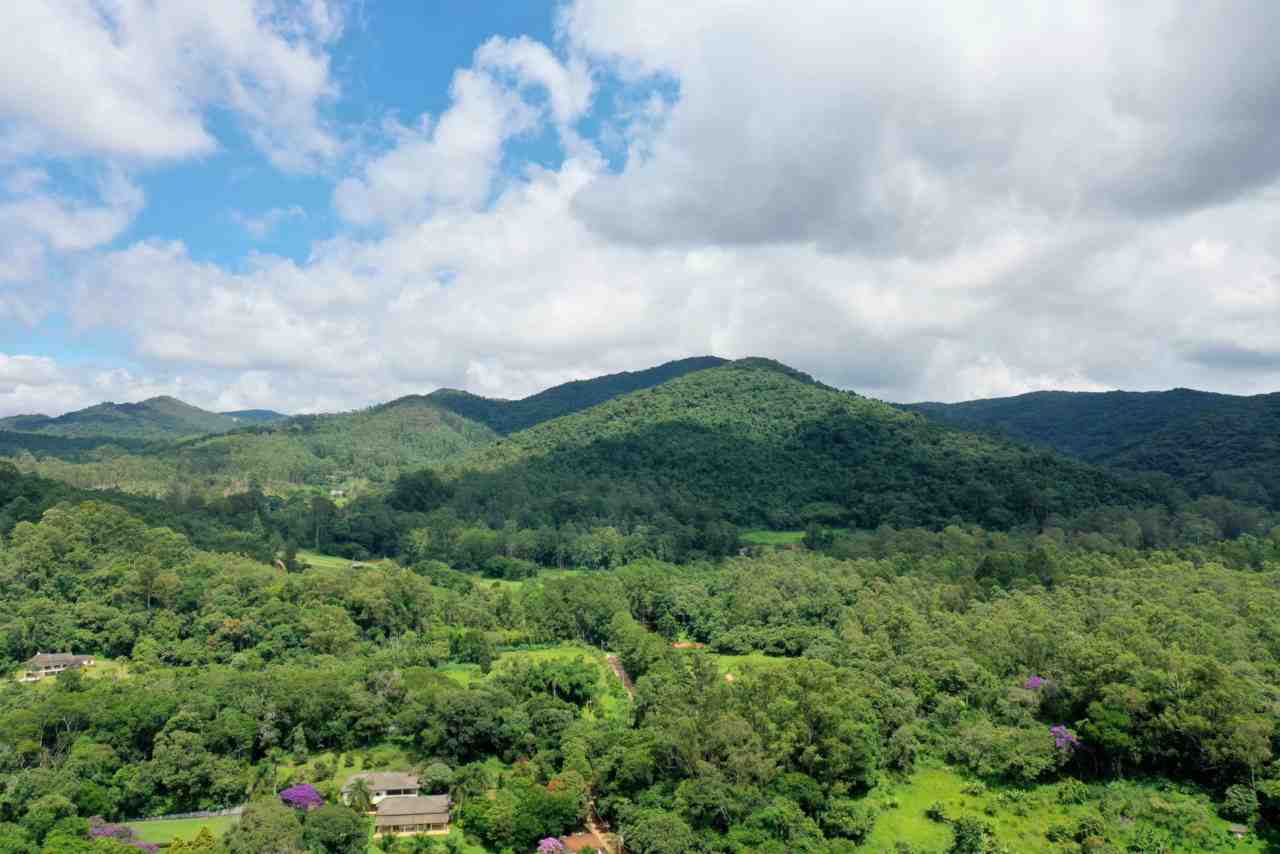 A Serra do Japi, localizada em Jundiaí - SP, exibe colinas verdes exuberantes sob um céu azul com nuvens brancas.