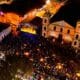Imagem aérea noturna do Festival de Inverno de Cabreúva 2024, com palco iluminado, multidão e igreja histórica ao fundo.