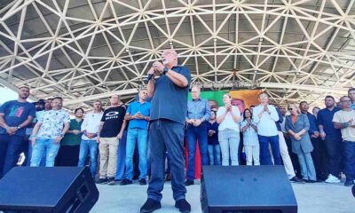 Dr. Luiz Braz discursando em convenção política, rodeado por apoiadores no palco coberto, promovendo sua reeleição em Campo Limpo Paulista.