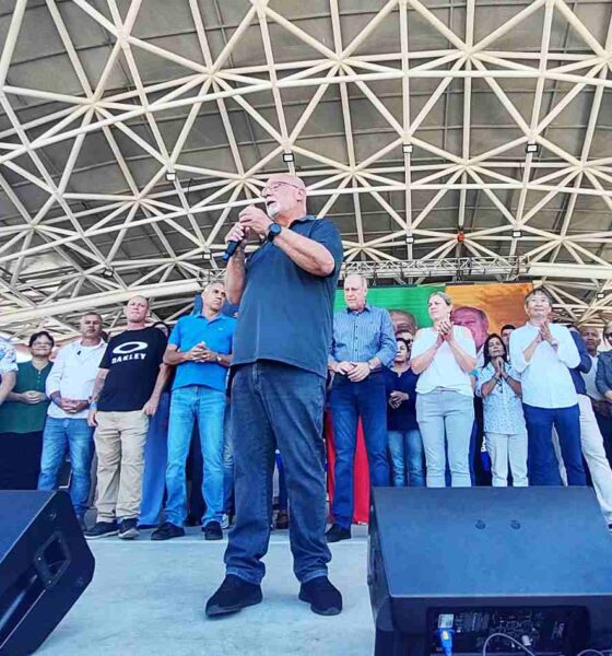 Dr. Luiz Braz discursando em convenção política, rodeado por apoiadores no palco coberto, promovendo sua reeleição em Campo Limpo Paulista.