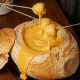 fondue de queijo servido dentro de um pão rústico, com garfos de fondue mergulhando pedaços no queijo derretido.