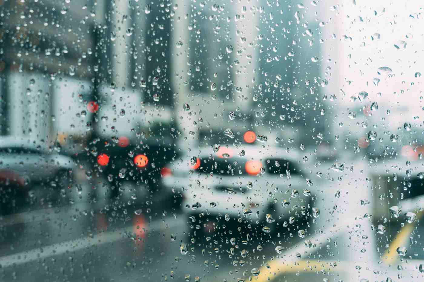 Carros embaçados pela chuva intensa vistos através de uma janela com gotas de água embaçando a visão.