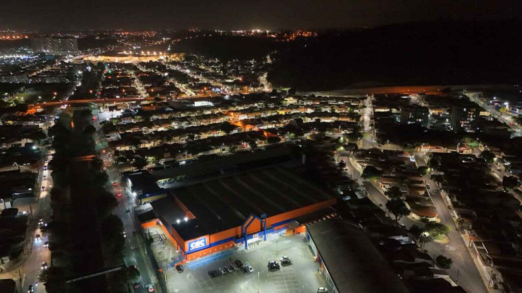 Vista aérea noturna de bairro residencial em Jundiaí com iluminação de lâmpadas de LED, destacando ruas e um grande centro comercial iluminado.