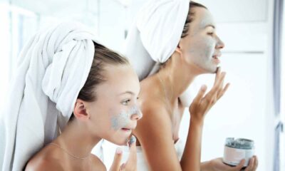 Menina e mulher aplicando máscaras faciais como parte da rotina de skincare em frente ao espelho, simbolizando cuidados com a pele.