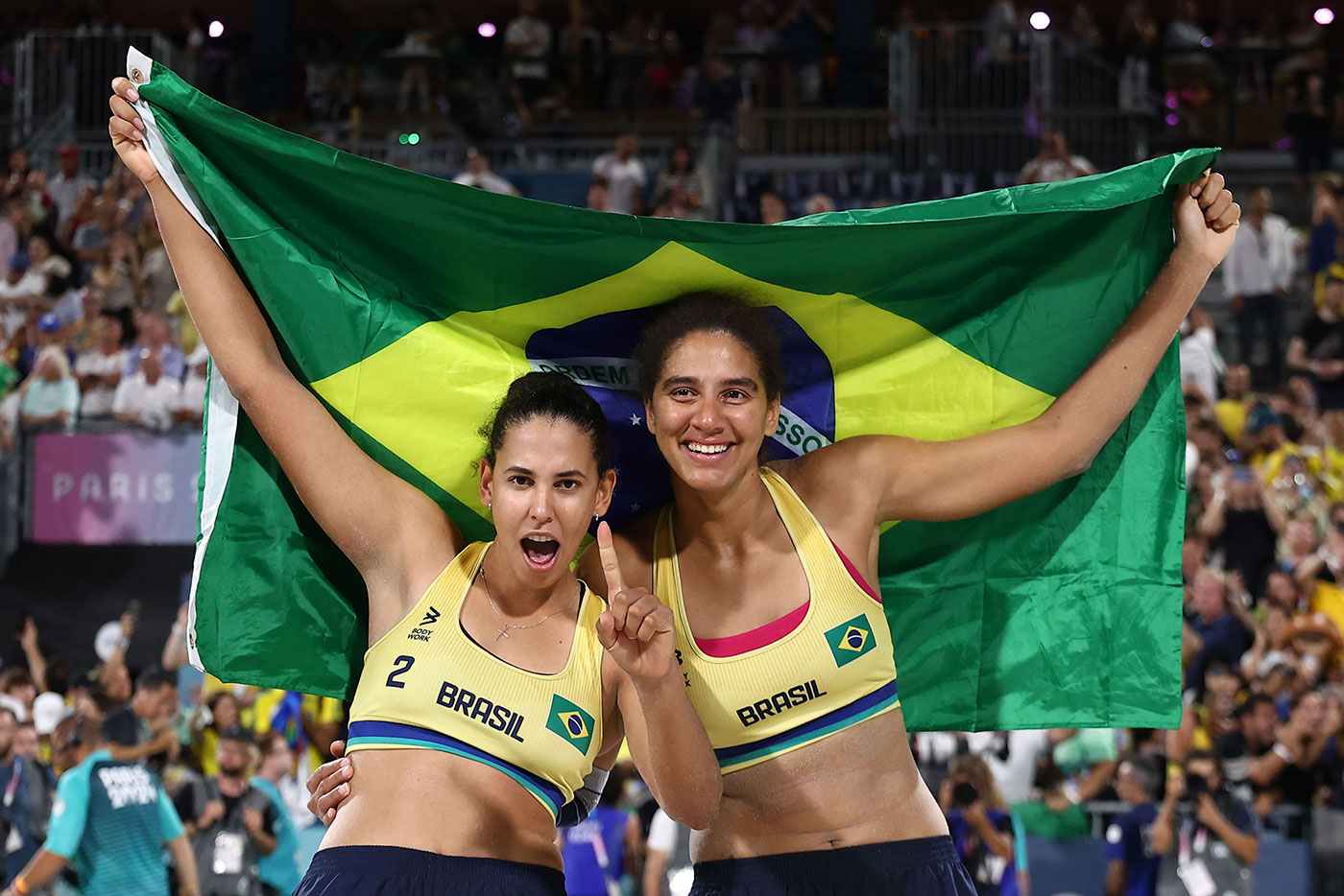 Duda e Ana Patrícia celebram a vitória com a bandeira do Brasil após conquistarem o ouro no vôlei de praia em Paris 2024.