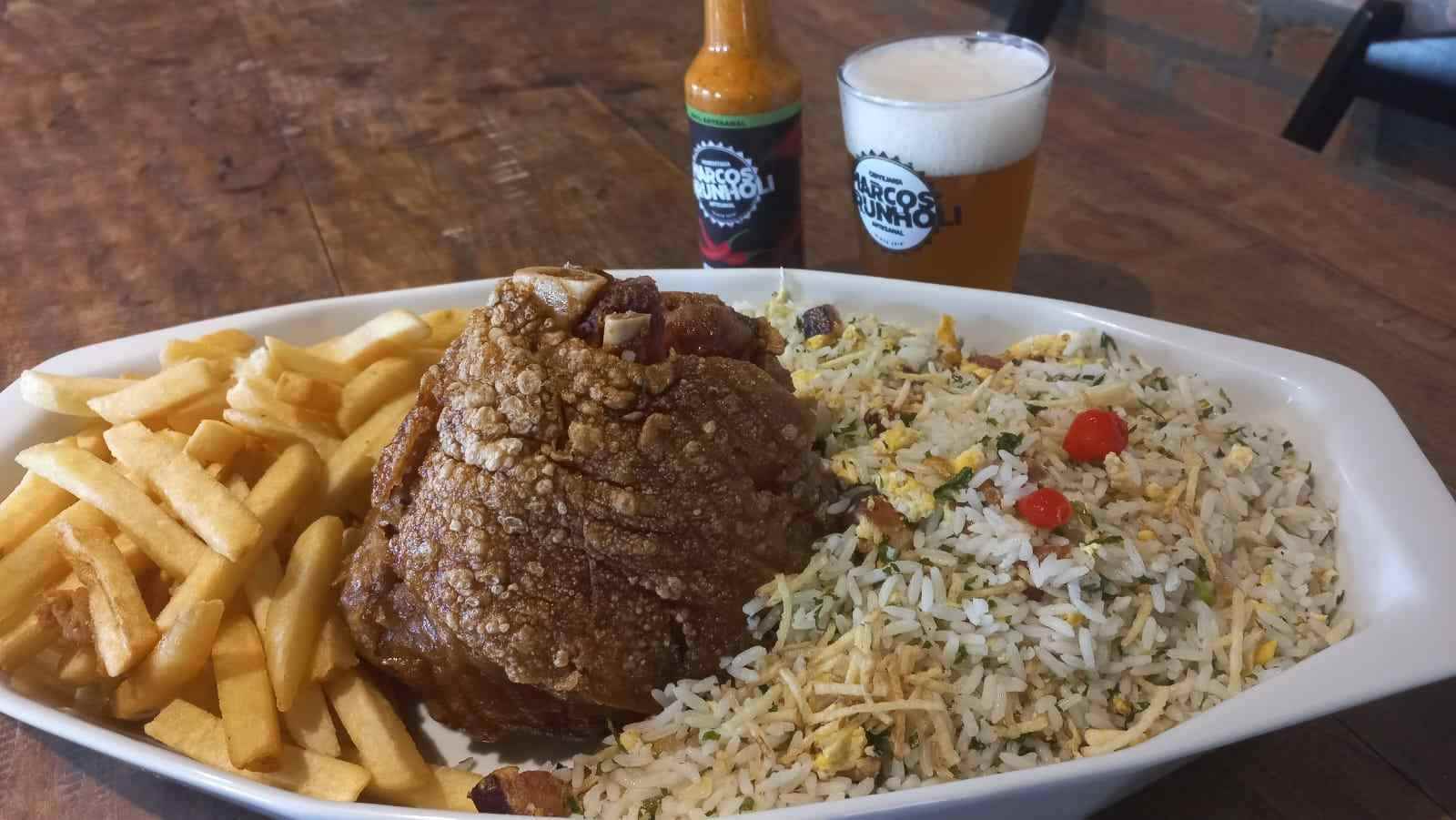 Joelho de porco crocante com arroz biro-biro e batatas fritas servido na Cervejaria Marcos Brunholi, acompanhado de cerveja artesanal.