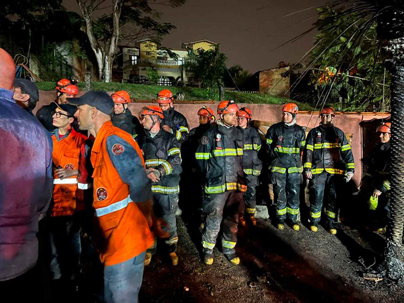 Equipe de bombeiros de SP reunida à noite em operação de resgate após acidente aéreo em Vinhedo, com uniformes e capacetes de segurança.