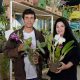 Casal exibe orquídeas na Festa das Orquídeas 2024, rodeados por diversas plantas em exposição no Clube de Campo da Cica.