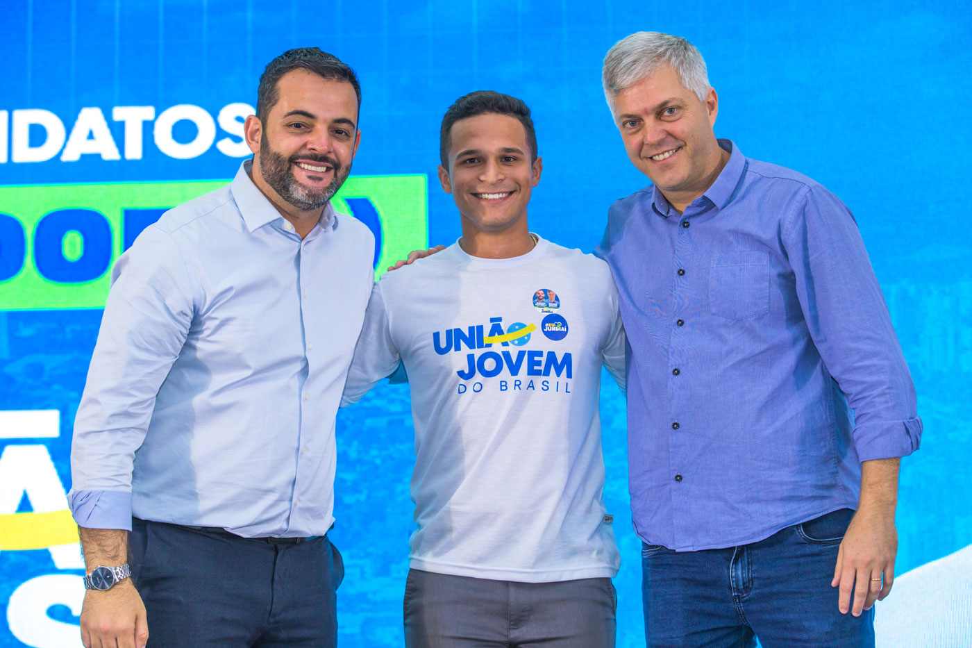 Gustavo Martinelli, Renan Peres e Ricardo Benassi sorrindo juntos em evento "Vozes da Cidade" em Jundiaí, com fundo azul e logo do União Brasil.