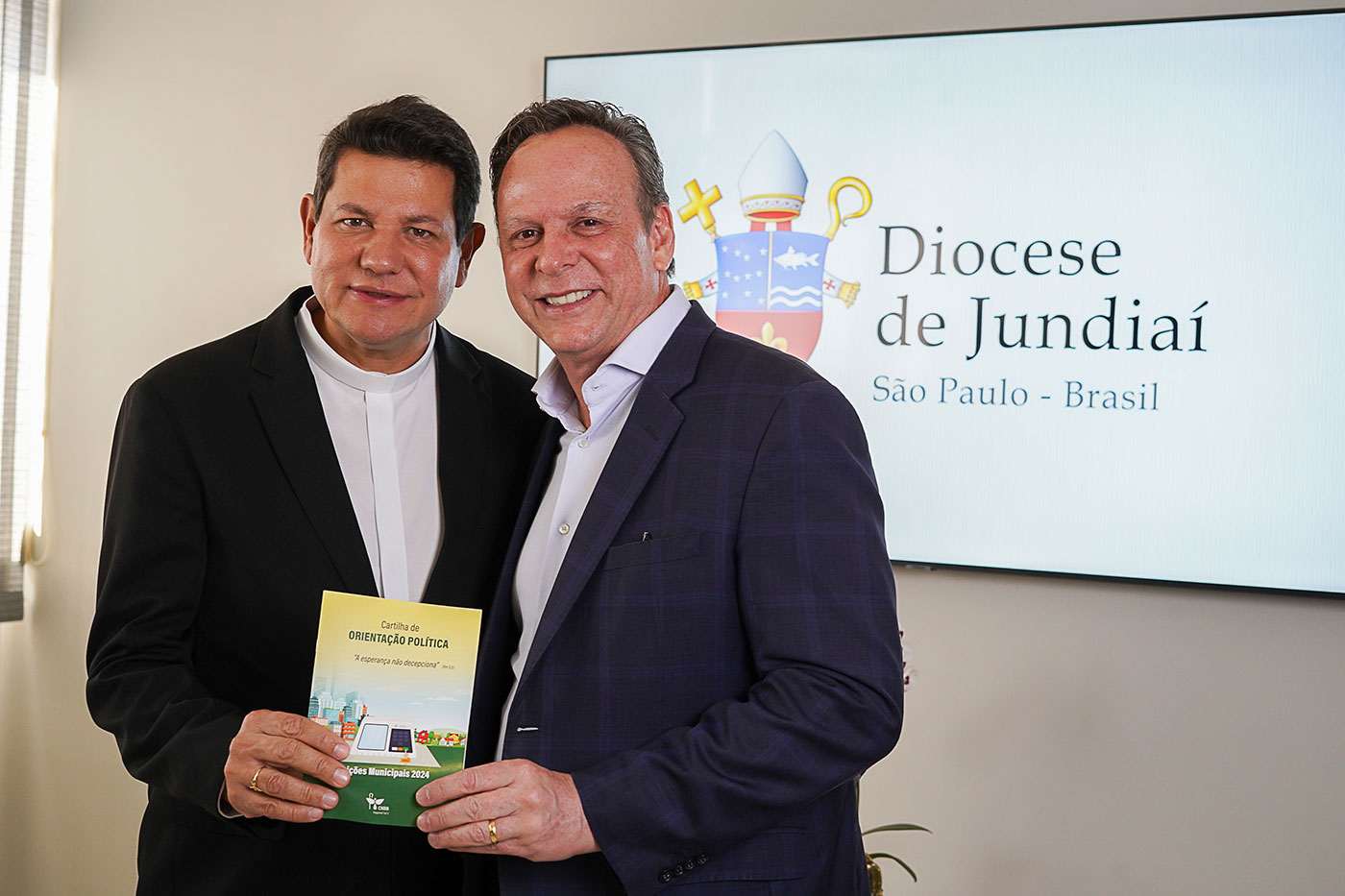 José Antonio Parimoschi e Padre Silvio Andrei posam com cartilha de orientação política na Diocese de Jundiaí.