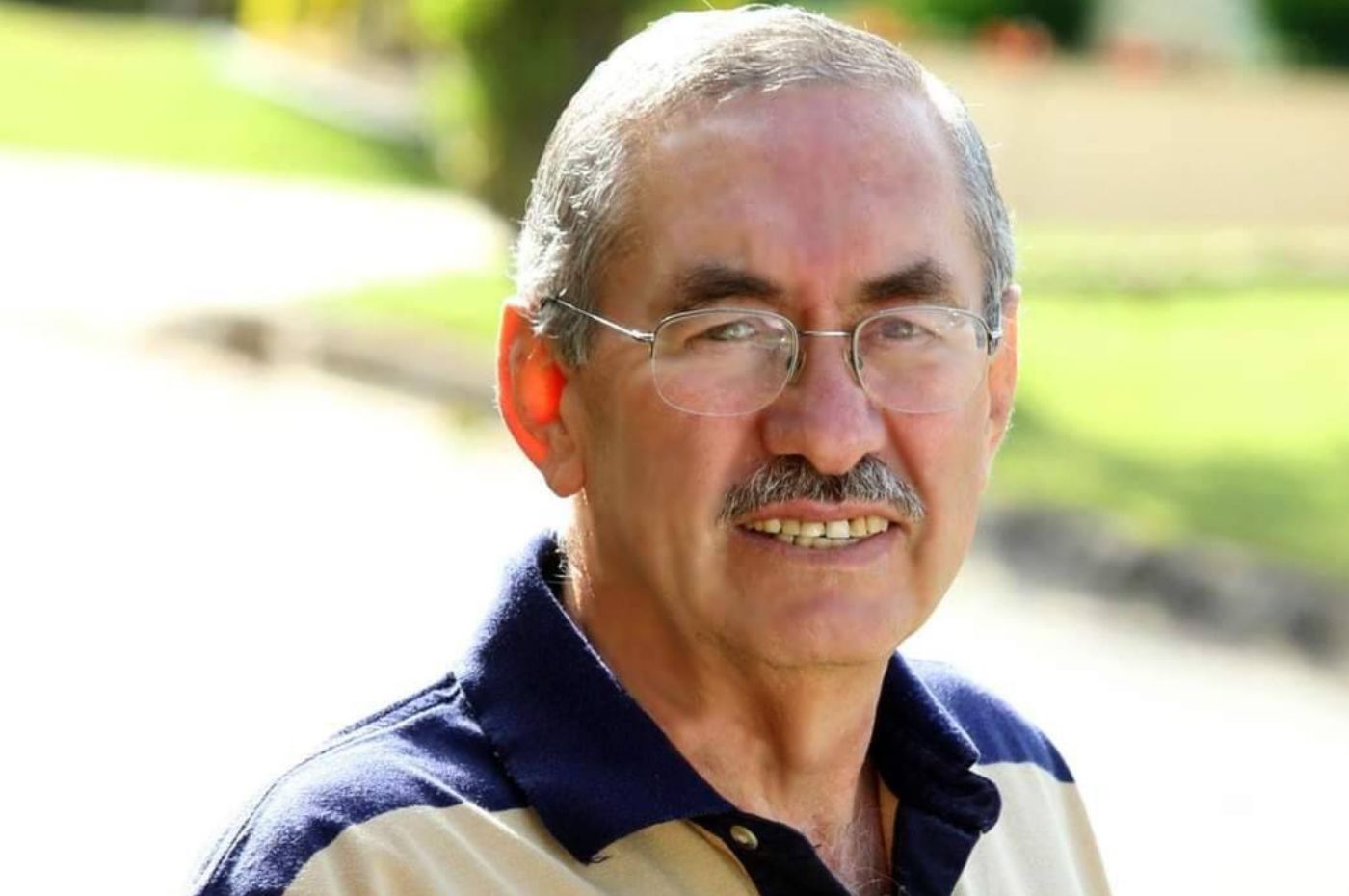 Retrato de Karmanghia, ex-prefeito de Louveira, sorrindo e usando óculos, com fundo ao ar livre em ambiente natural.