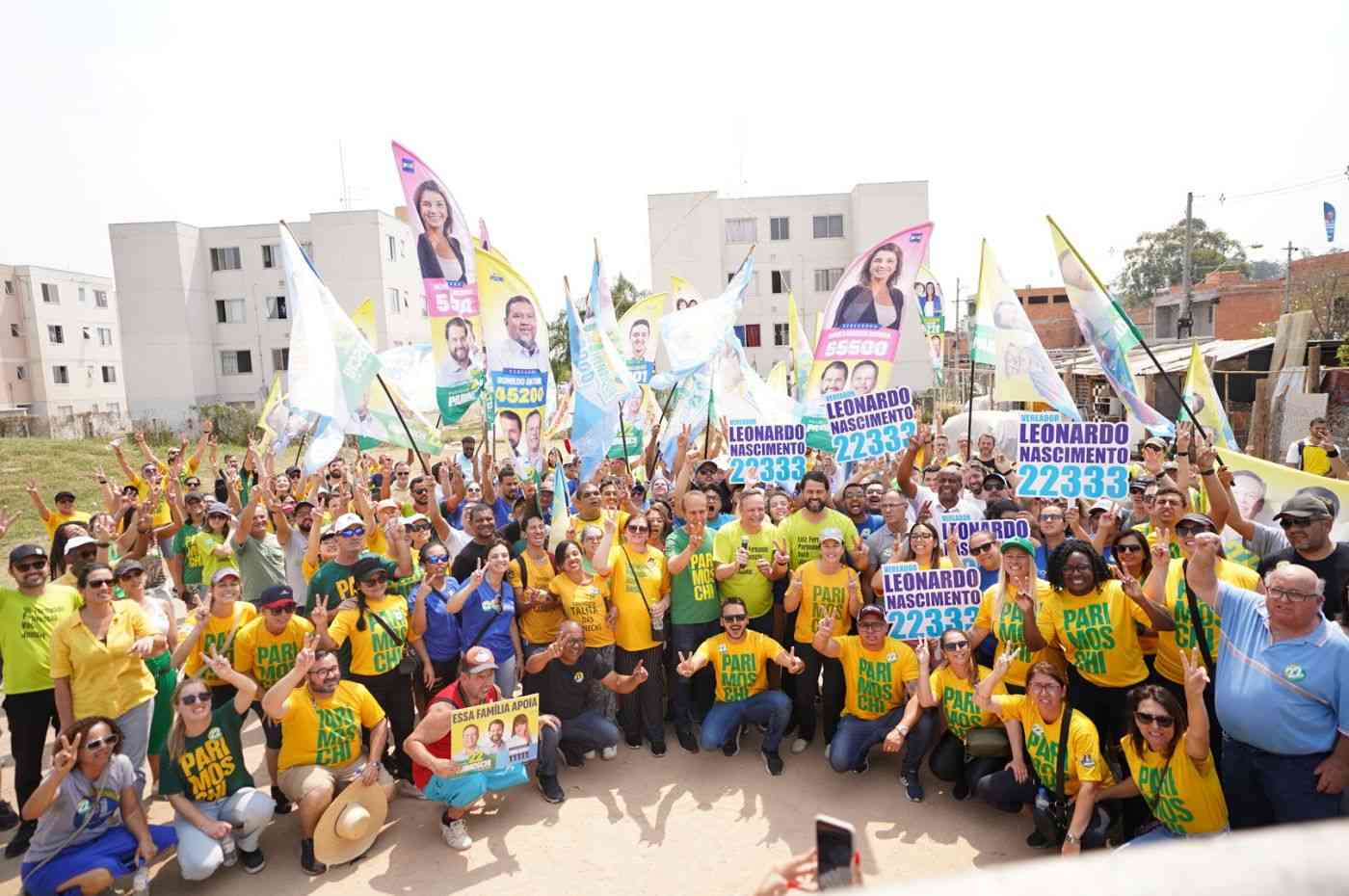 Grupo de apoiadores de Parimoschi em caminhada de campanha no Jardim Novo Horizonte, segurando bandeiras e cartazes de candidatos aliados.