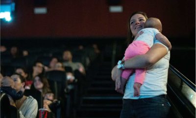 Mulher com bebê no colo assiste a sessão CineMaterna no cinema, ambiente acolhedor e adaptado para famílias com crianças