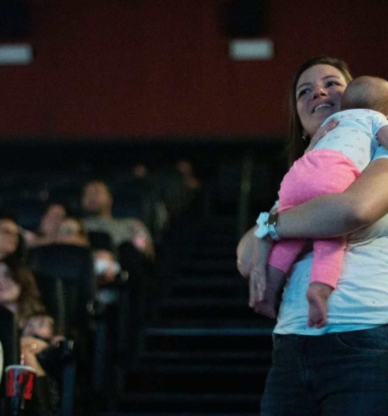 Mulher com bebê no colo assiste a sessão CineMaterna no cinema, ambiente acolhedor e adaptado para famílias com crianças